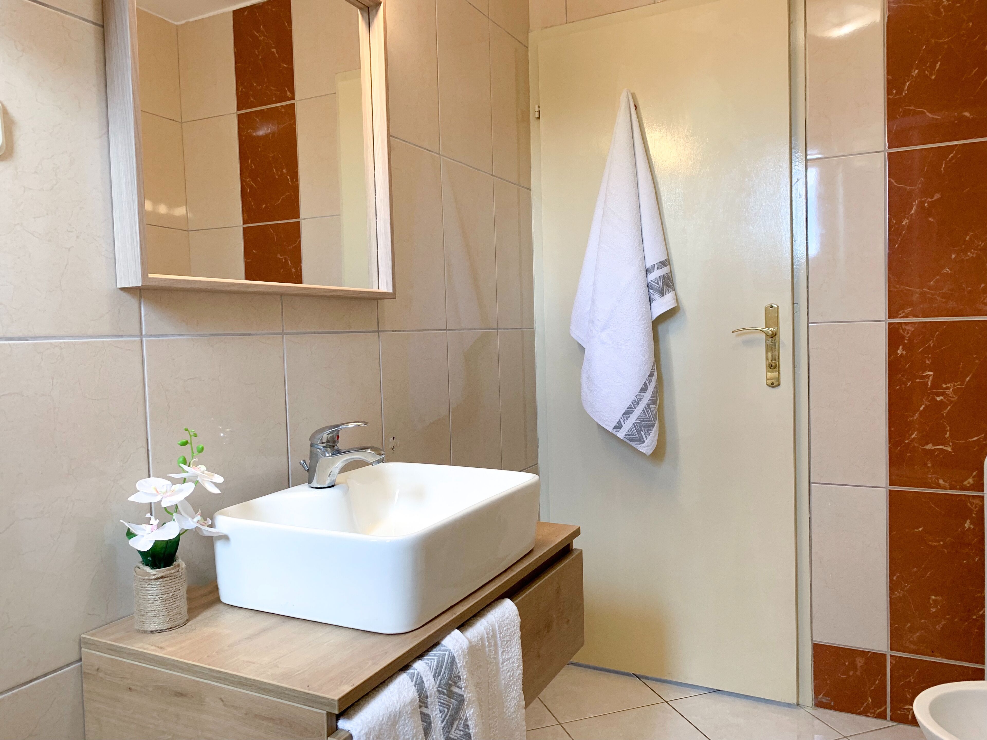 Un baño con un lavamanos blanco, una toalla colgada en la pared y un espejo sobre el lavamanos.