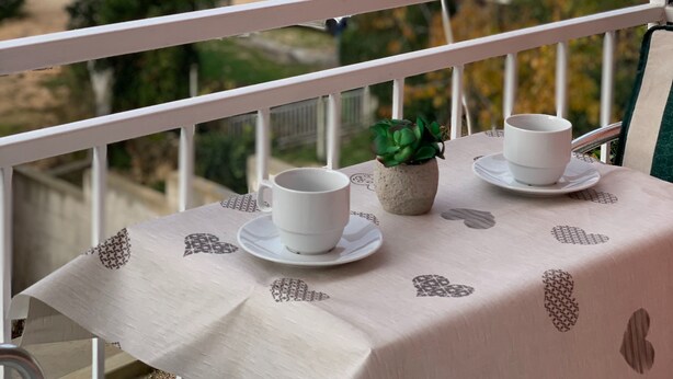 A balcony with a table set for two, overlooking a residential area with houses and trees.