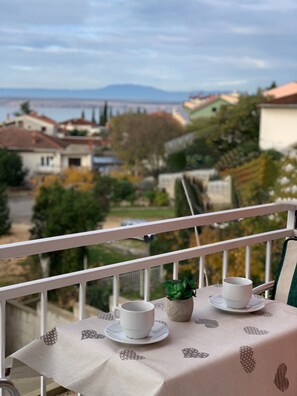 Un balcone con un tavolo apparecchiato per due persone, con vista su una zona residenziale con case e alberi.