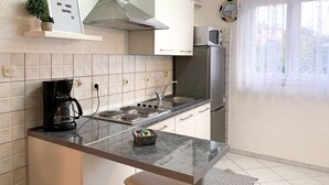 A modern kitchen with a stainless steel stove, microwave, and refrigerator. There is a small plant on the wall and a clock on the wall.