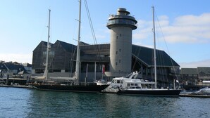 A lighthouse with a cylindrical tower and a flat roof, adjacent to a dock with two boats. - Romantic Retreat (Penryn)