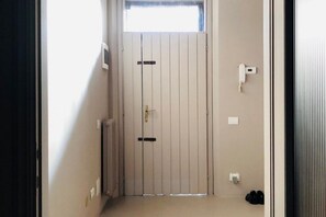 Un couloir étroit, avec une porte au fond, une petite fenêtre au-dessus de la porte et un téléphone fixé au mur.