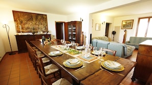 Une salle à manger avec une longue table en bois, dressée pour le repas, et des chaises disposées de part et d’autre.