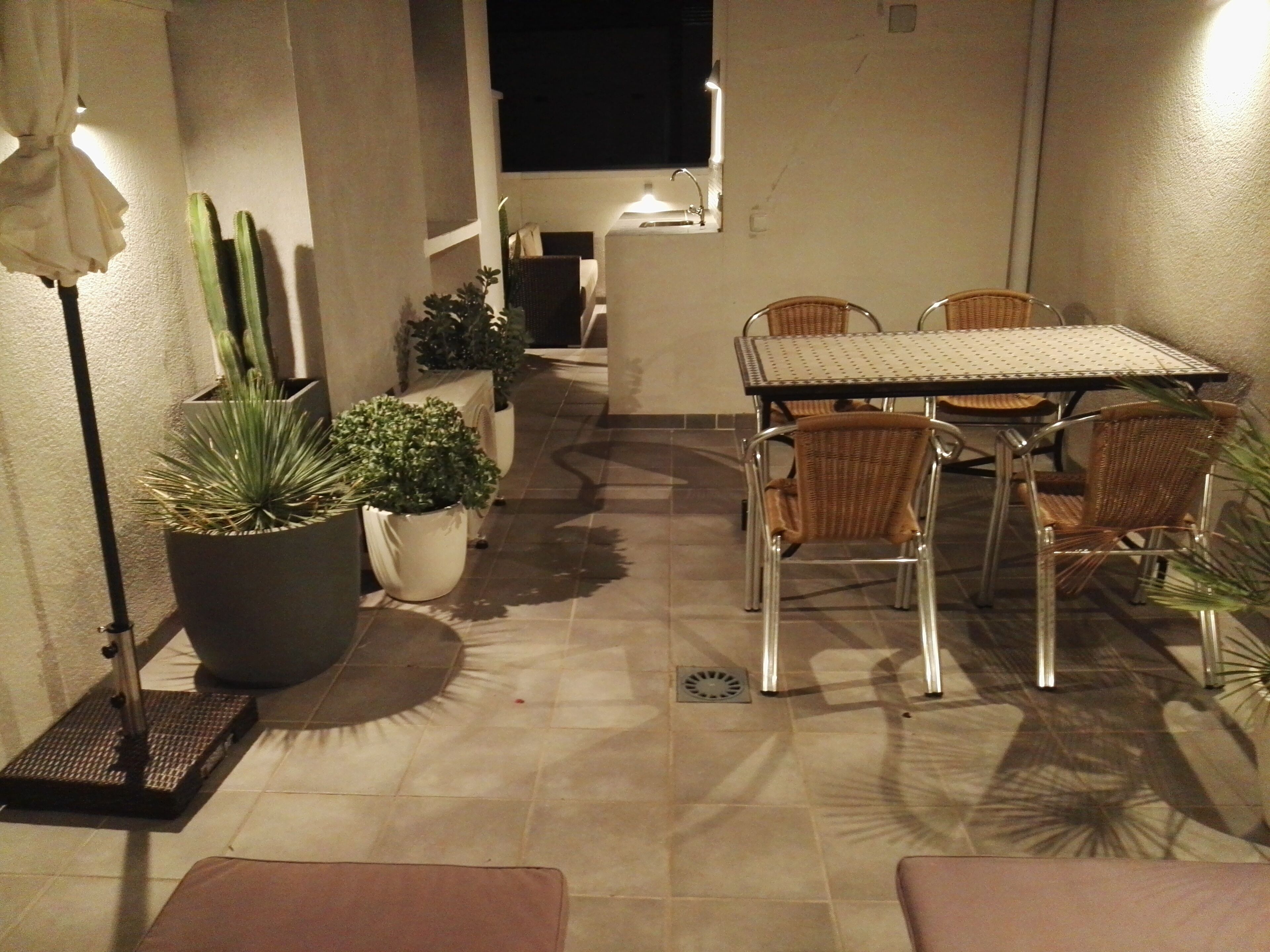 An outdoor patio area with a table and chairs, potted plants, and a floor lamp.