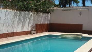 A rectangular swimming pool with a tiled edge, surrounded by a low wall with a white and brown color scheme, and trees in the background.