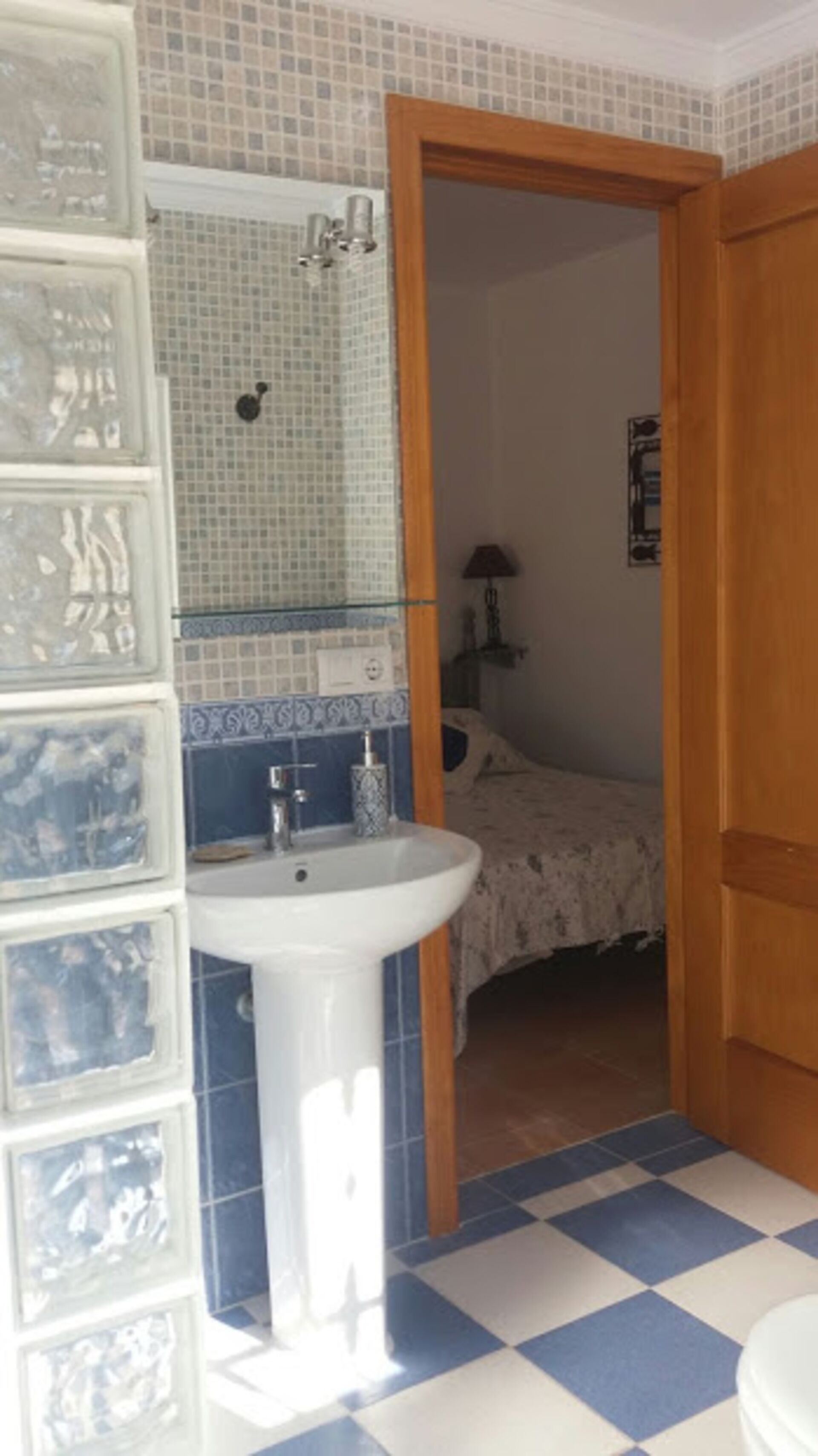 A bathroom with a white sink, blue and white checkered floor, and a mirror with mosaic tiles.