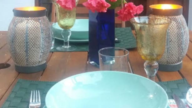 Una mesa de comedor dispuesta con platos, un florero y dos velas encendidas.