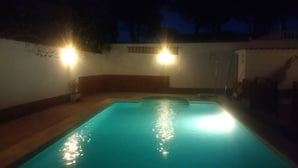 Una piscina por la noche con dos luces fijadas a la pared.