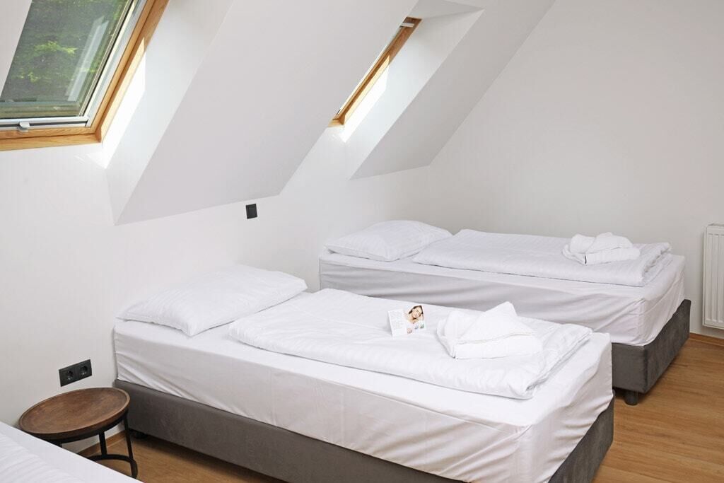 Une chambre avec deux lits, un petit tabouret et une lucarne.