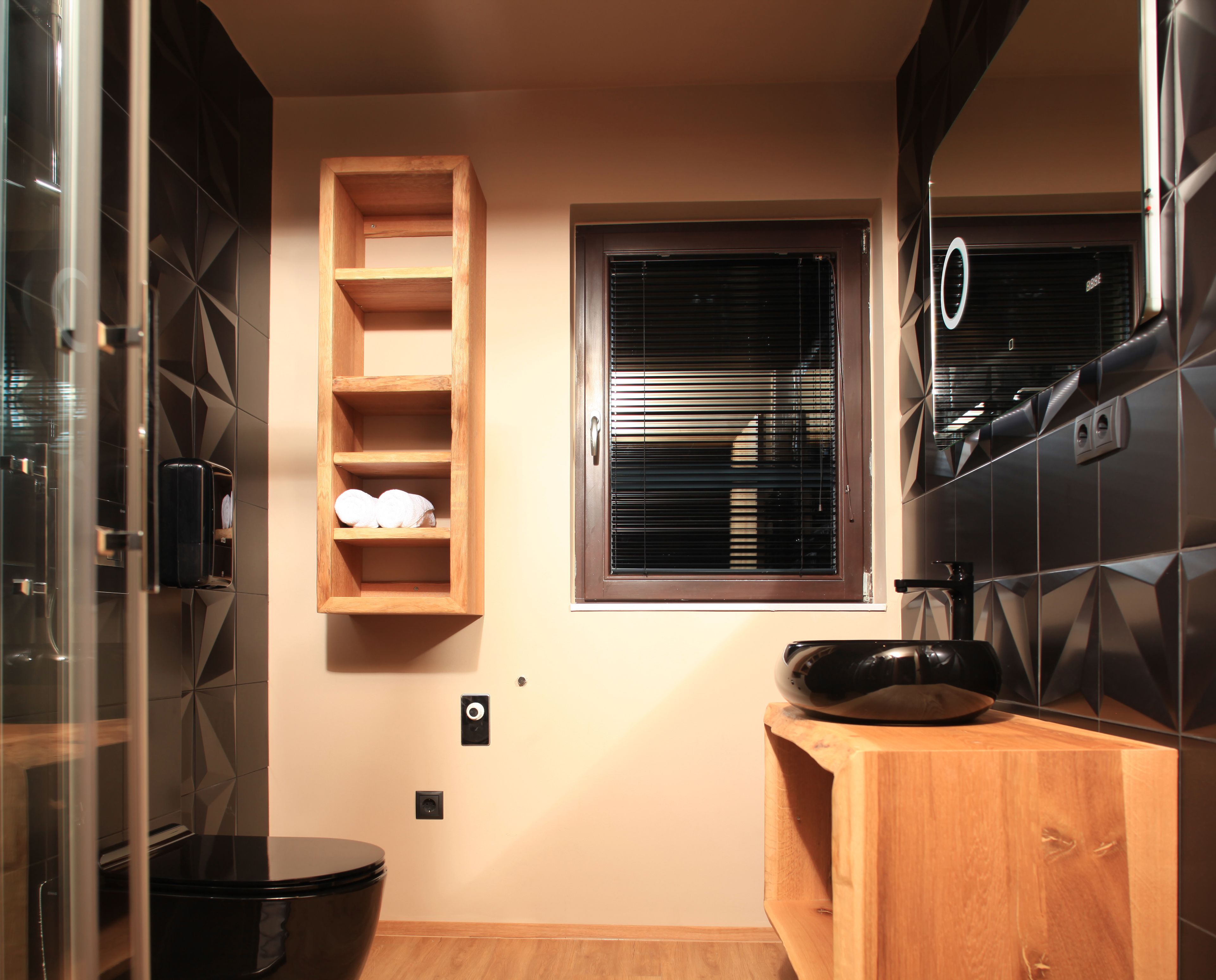 A compact bathroom with a wooden vanity, a black toilet, and a window with blinds.