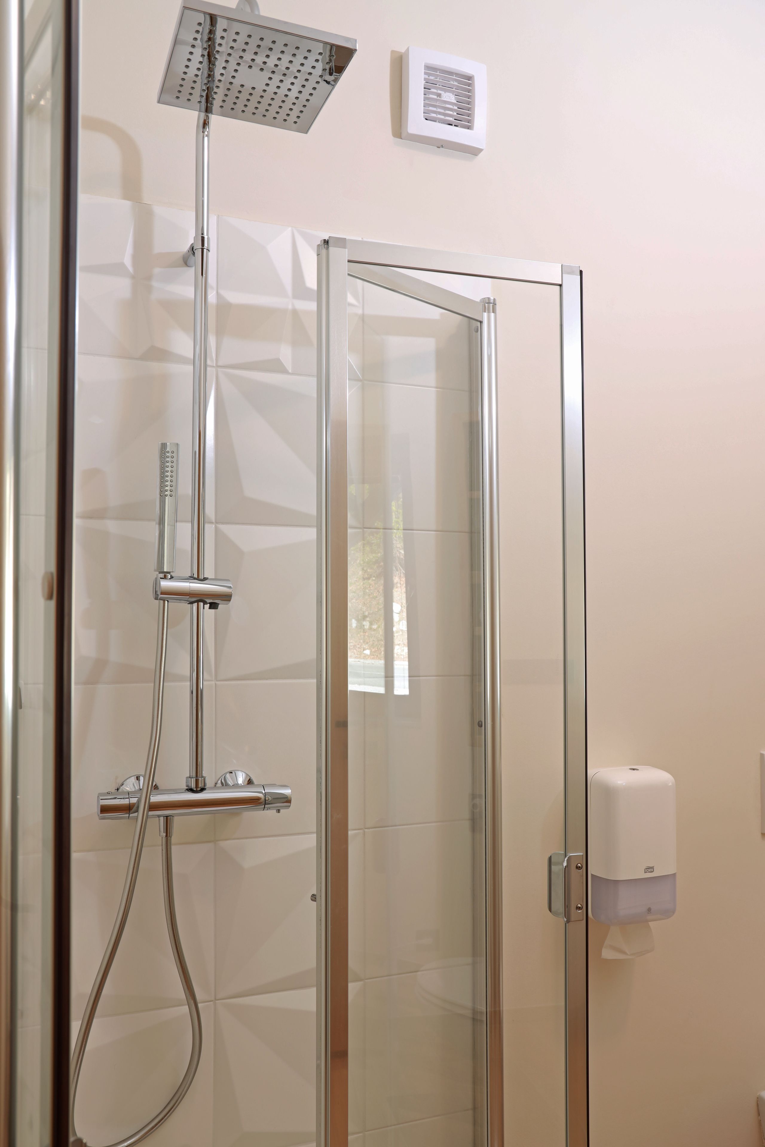 Une douche fermée par des parois en verre, dotée d’un pommeau de douche à main et d’un panneau de commande fixé au mur.
