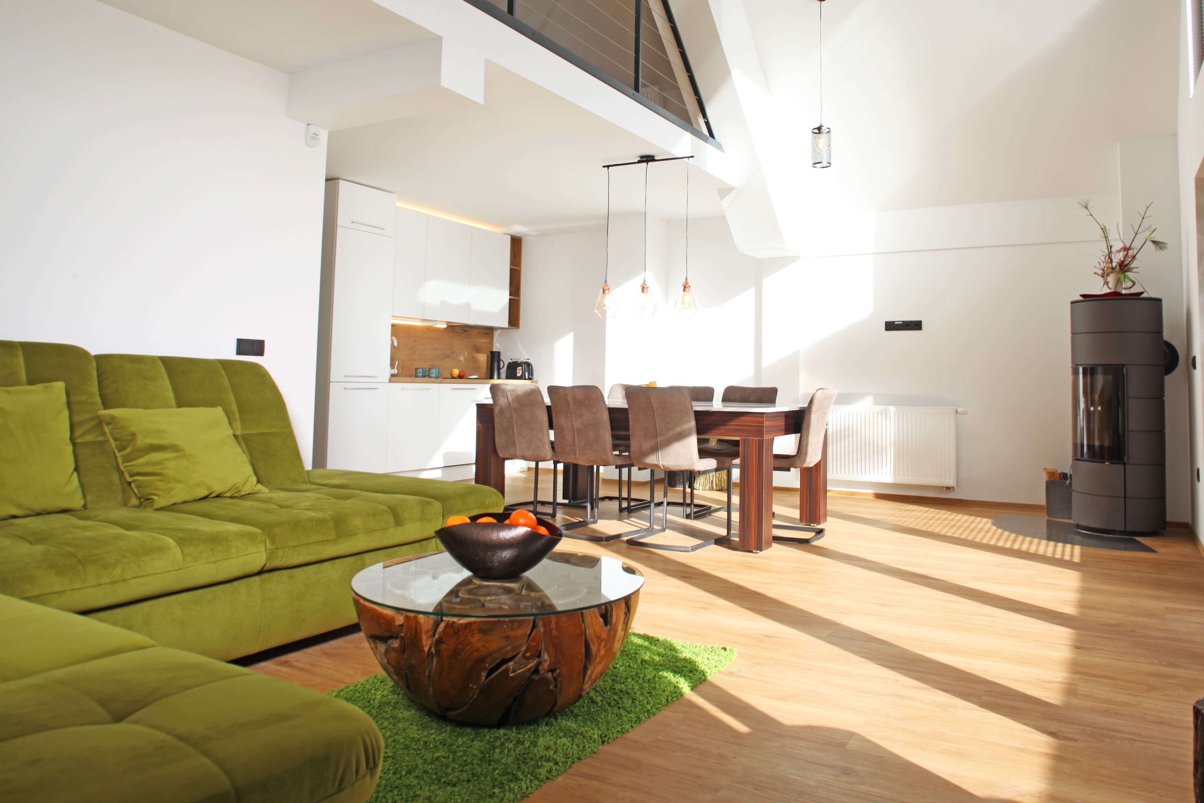 Una sala de estar moderna con un sofá verde, una mesa de centro de vidrio y un comedor con sillas y una mesa de madera.