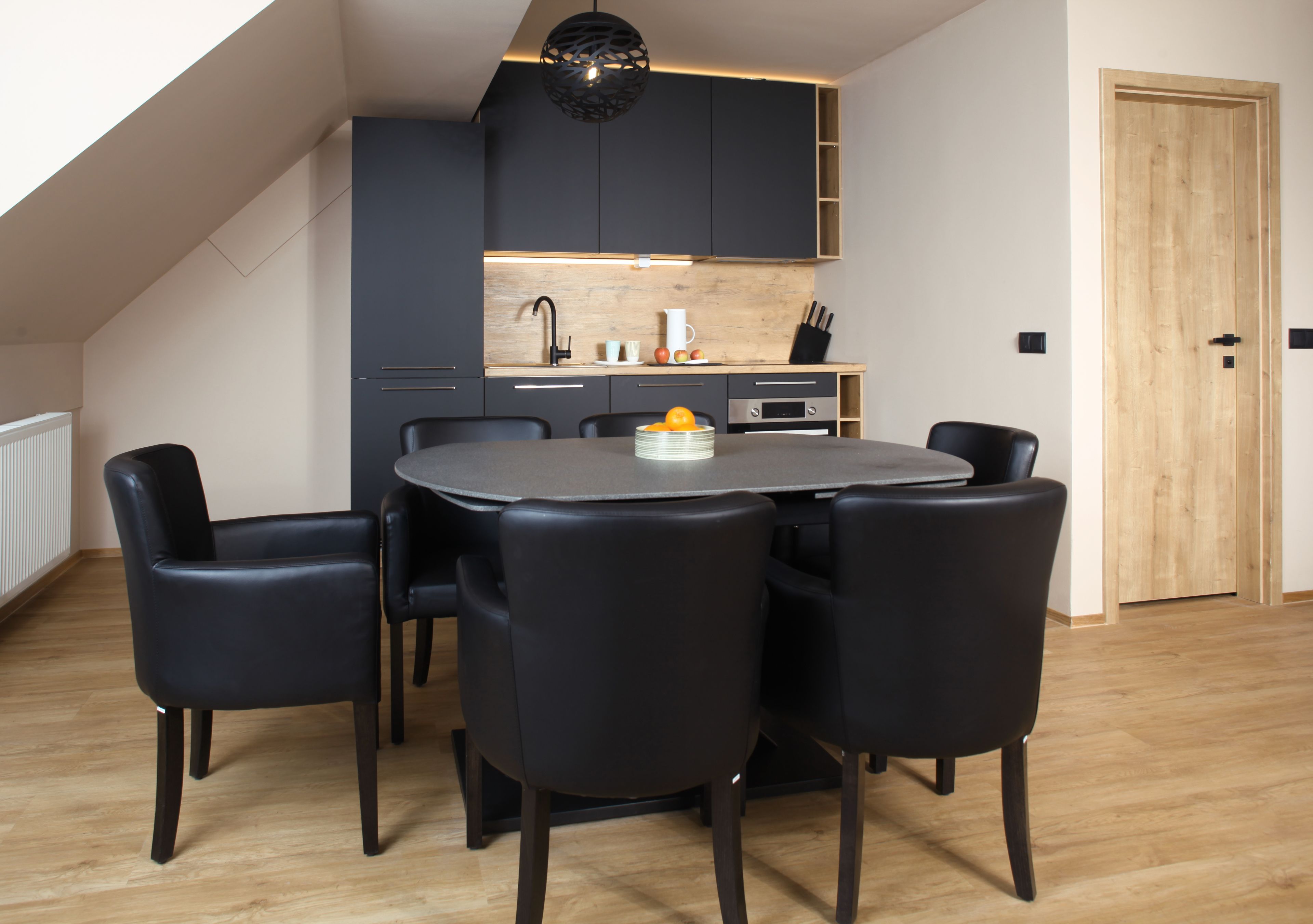 A modern kitchen with dark cabinets, a wooden countertop, and a dining area with a round table and black chairs.