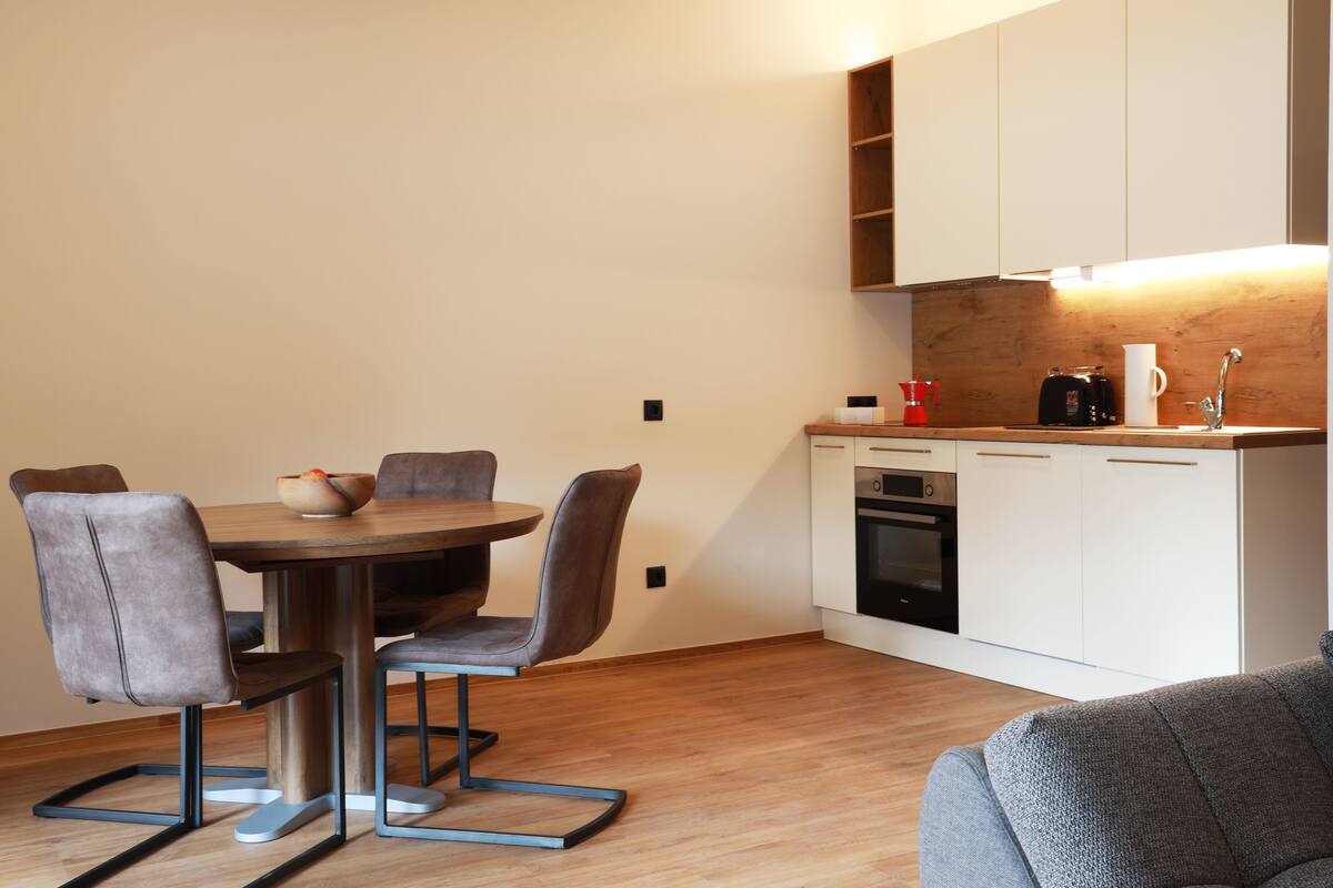 A compact kitchen with a dining area, featuring a round table, chairs, and modern appliances.
