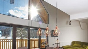 Et moderne køkken med et stort spisebord, hængende lamper og udsigt til et sneklædt landskab gennem store vinduer.