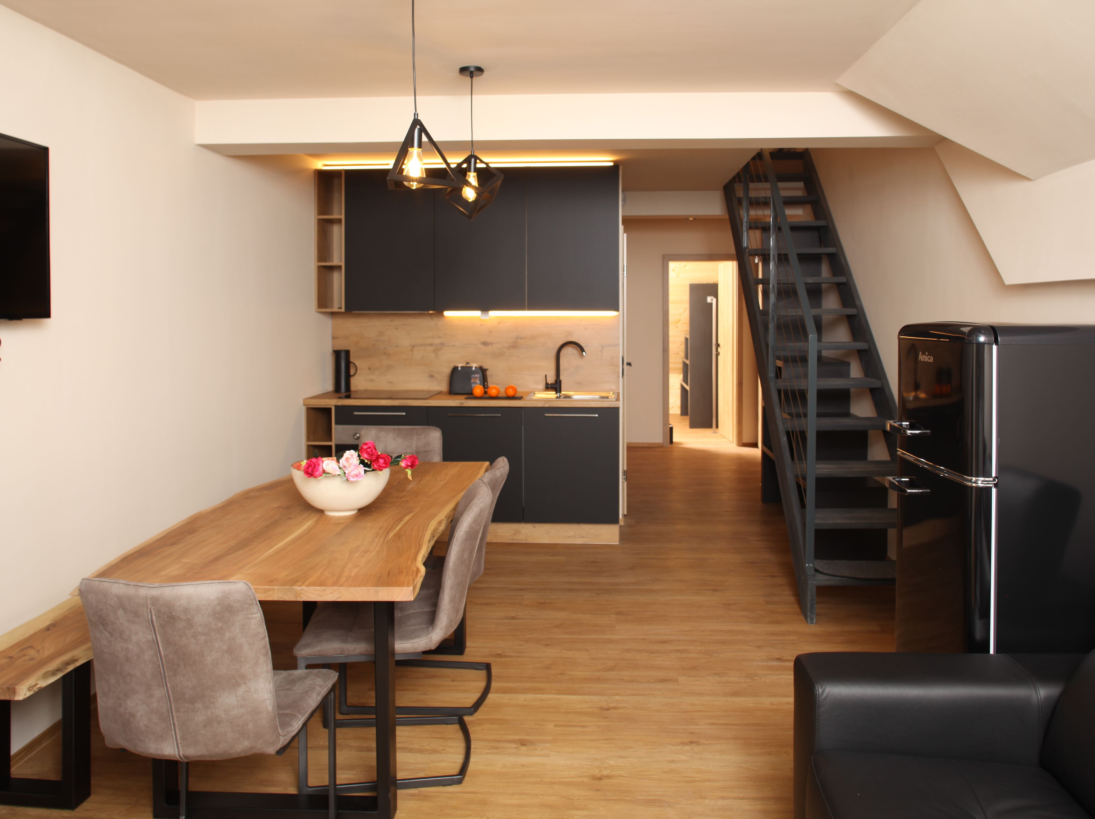 A modern kitchen with dark cabinets, a wooden dining table, and a black staircase.