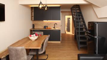 A modern kitchen with dark cabinets, a wooden dining table, and a black staircase.