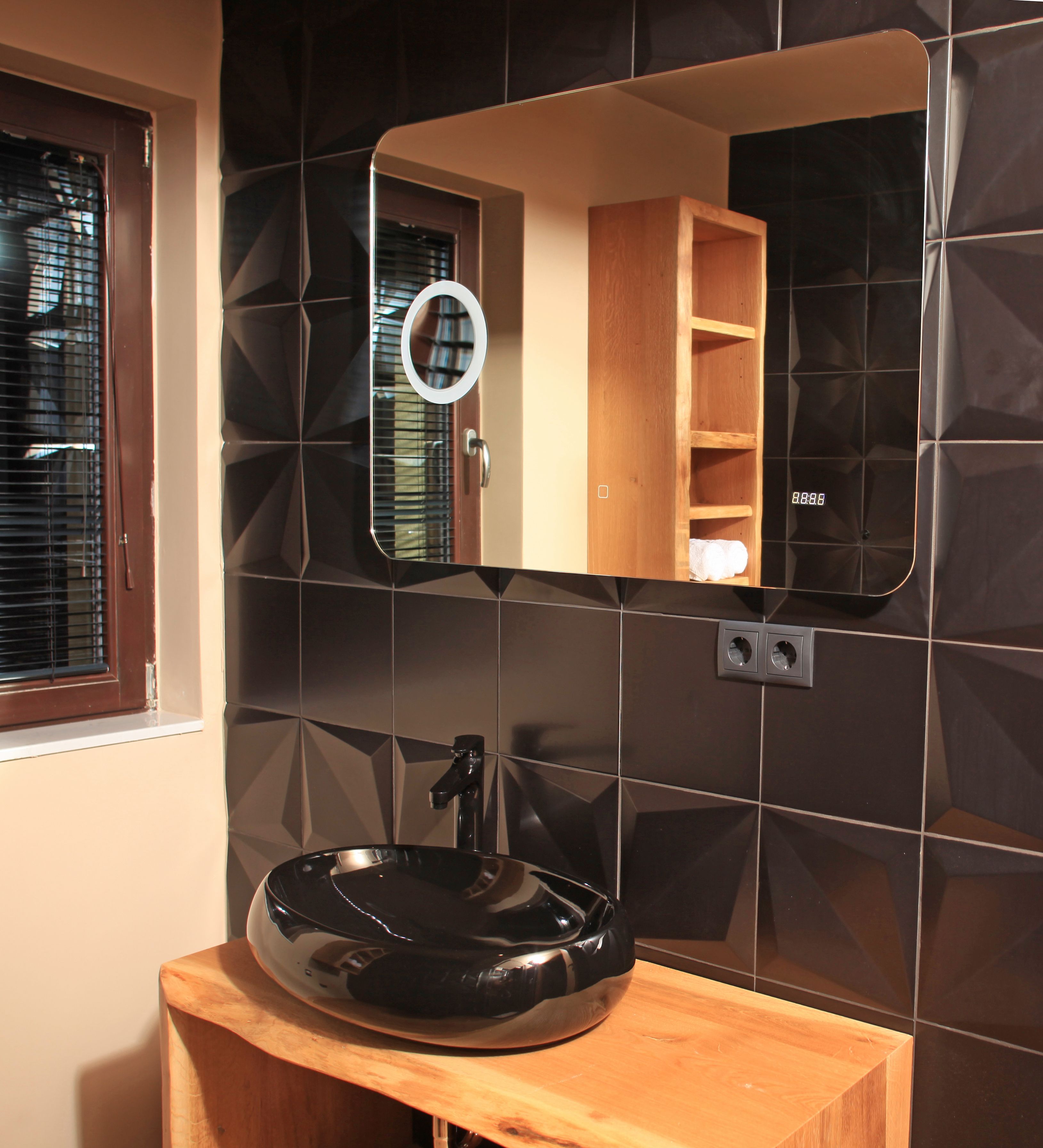 A bathroom with a black sink, a mirror, and a wooden shelf above the mirror.
