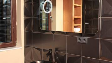 A bathroom with a black sink, a mirror, and a wooden shelf above the mirror.
