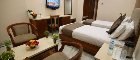A hotel room with two beds, a desk with a chair, a television, and a small table with a vase of flowers.