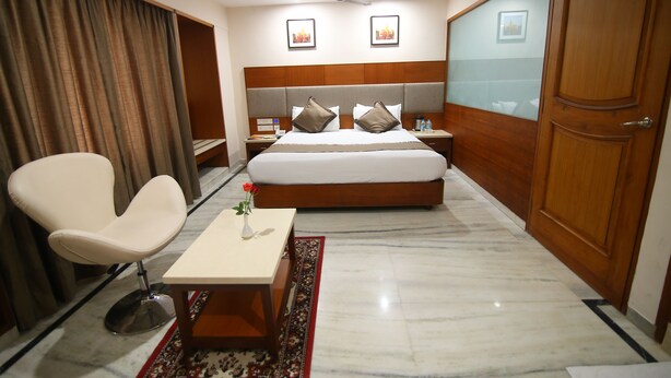 A hotel room with a bed, a chair, a nightstand, a table, and a wardrobe. - Daspalla Executive Court (Visakhapatnam)