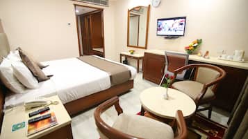 Habitación de hotel con cama, escritorio con teléfono y controles remotos, una mesa redonda con sillas, televisor y espejo.