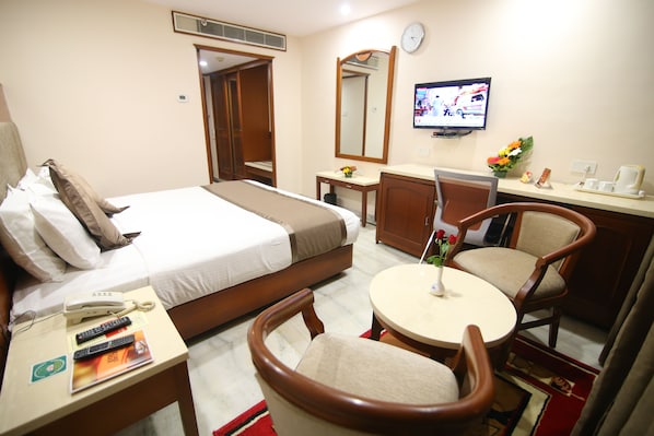 A hotel room with a bed, a desk with a telephone and remote controls, a round table with chairs, a television, and a mirror. - Daspalla Executive Court (Visakhapatnam)