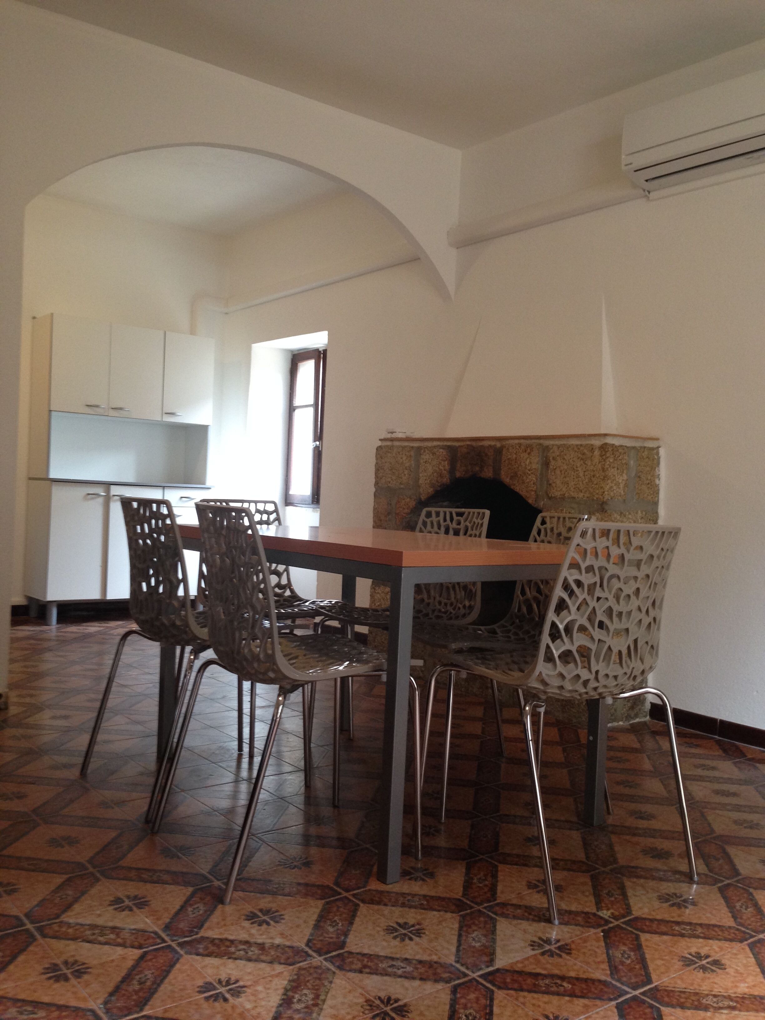 A dining area with a table and chairs, a kitchen in the background, and a tiled floor.