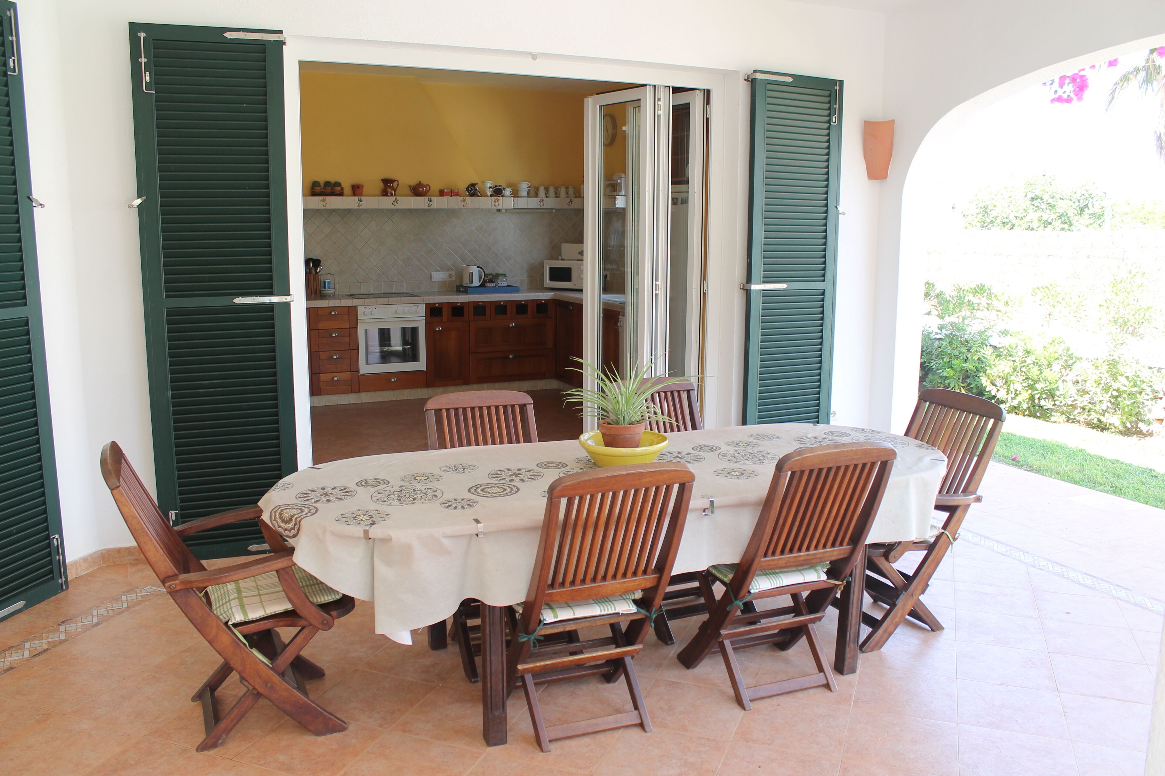 A dining area with a round table, six wooden chairs, and a potted plant on the table.