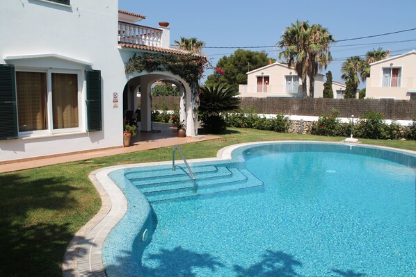 A swimming pool with a clear blue water, surrounded by a well-maintained lawn and a white building with a balcony.