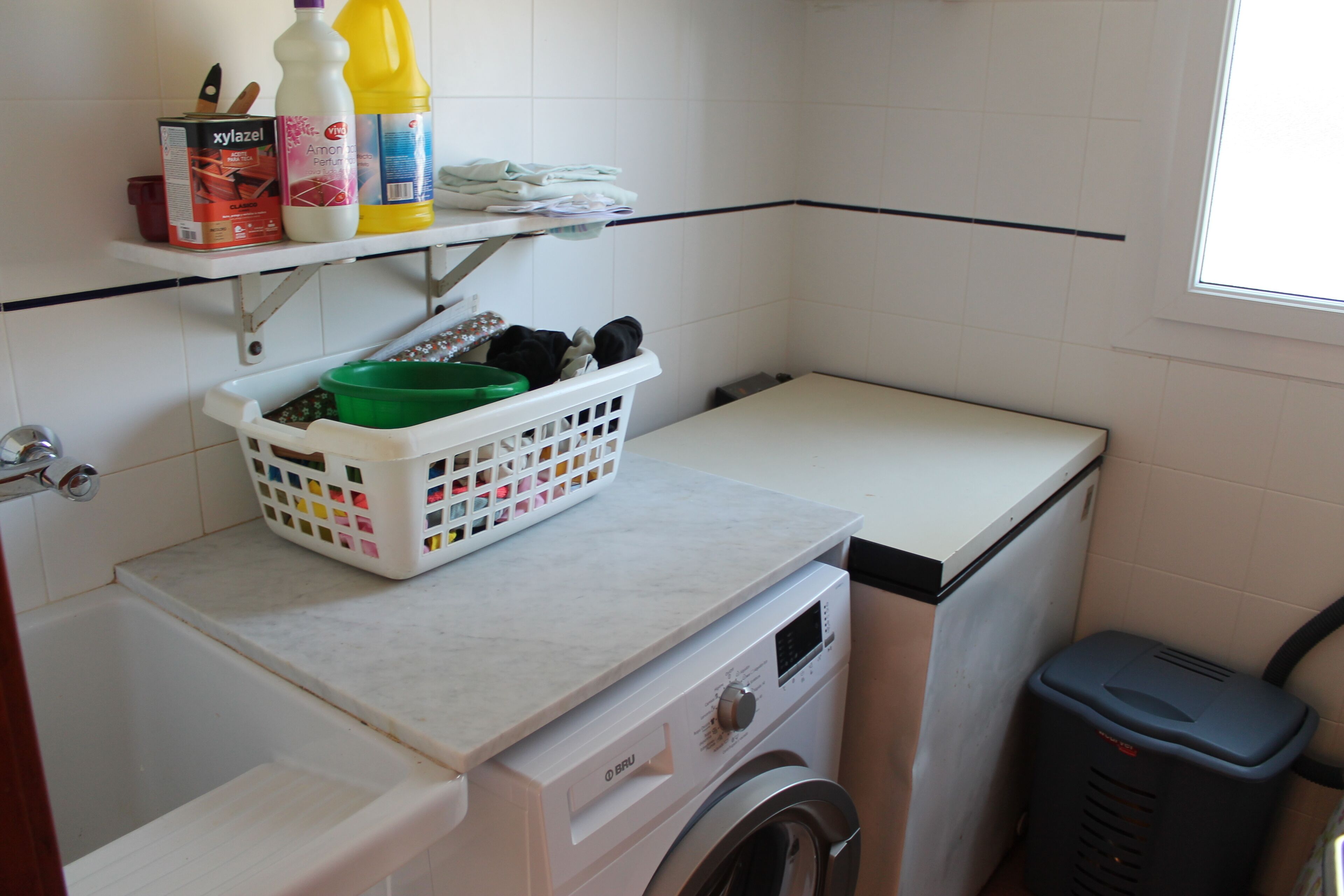 Un espacio de lavandería compacto con lavadora, secadora, estante con productos de limpieza y cesto de ropa.