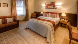 A hotel room with a bed, a sofa, a chair, a nightstand with a lamp, and a framed picture on the wall. - Castle Inn (Strabane)