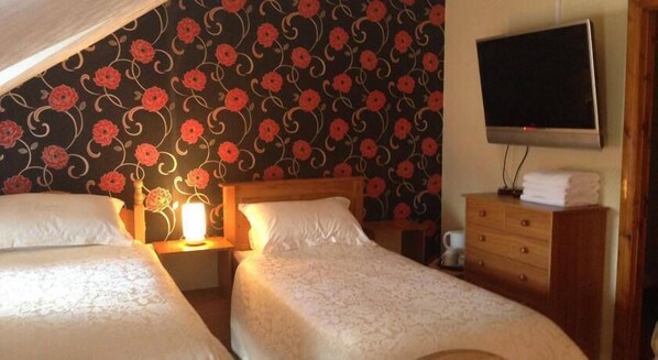 A room with two beds, a wooden dresser, a flat-screen TV, and a wall with a floral pattern.