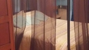 Une chambre avec un lit sous un dais, un plancher en bois et une lampe sur une table de chevet.