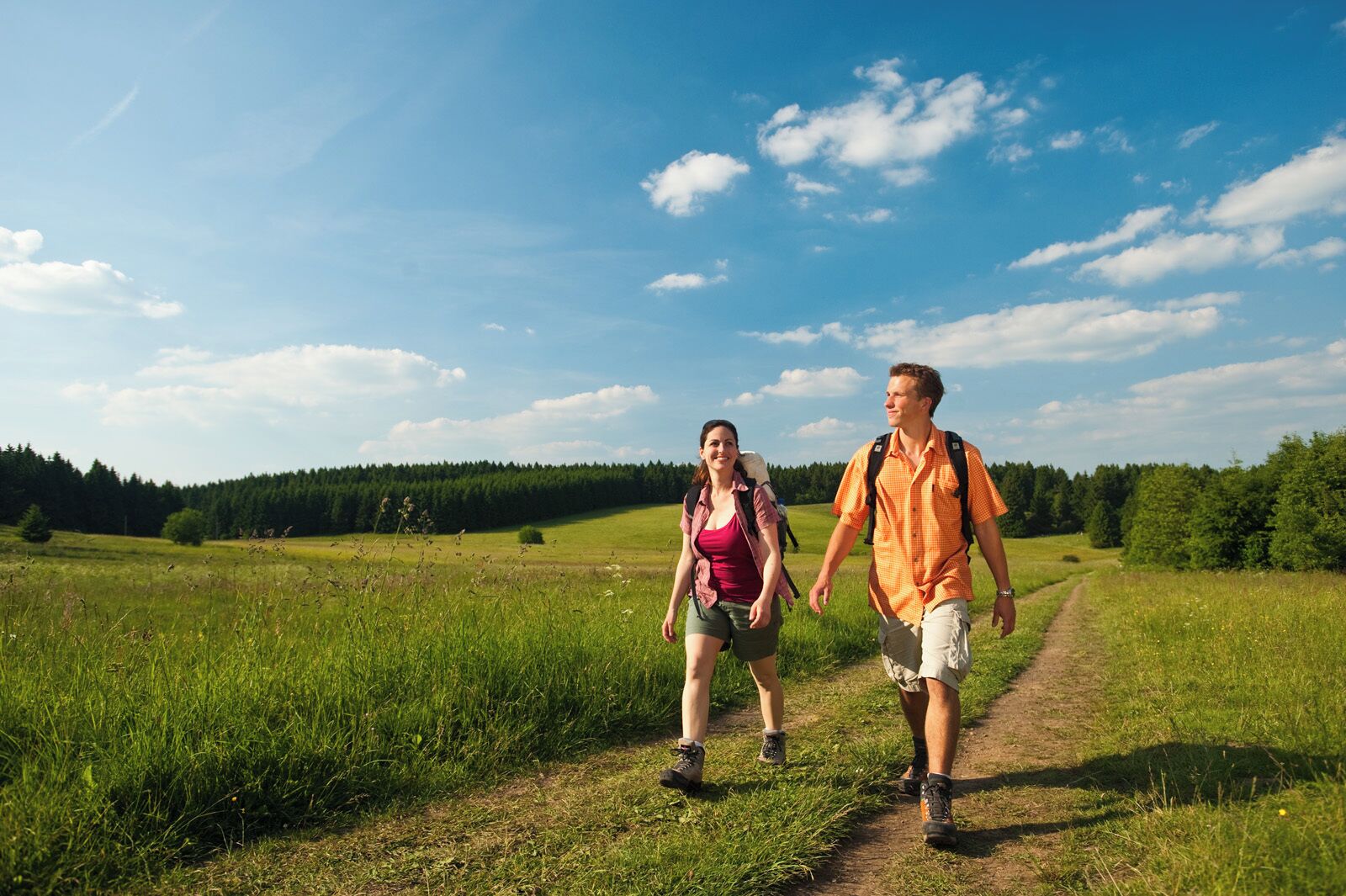 Zwei Personen laufen auf einem Feldweg durch ein grasbewachsenes Feld, im Hintergrund Bäume.