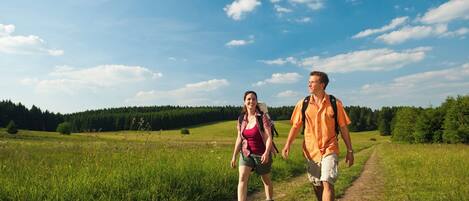 Two people walking on a dirt path in a grassy field with trees in the background.