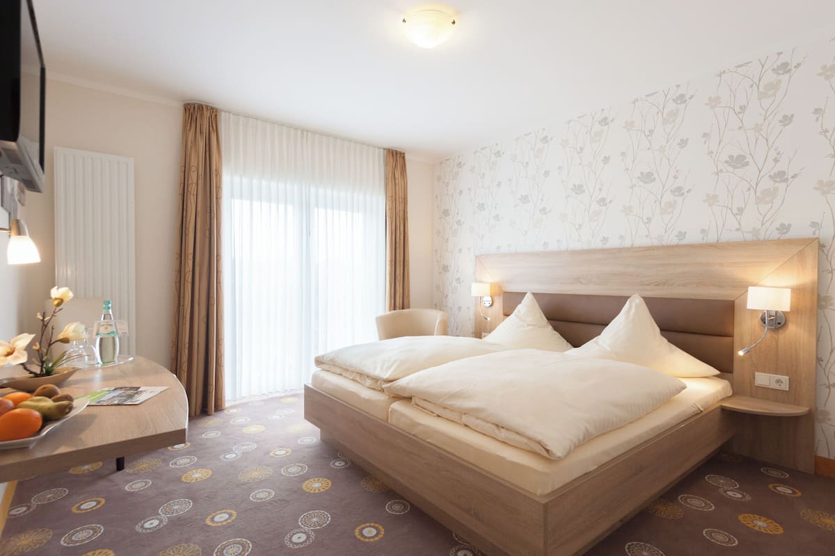 Ein Hotelzimmer mit einem großen Bett, Nachttischen, einem Schreibtisch mit Stuhl, einem Heizkörper und einem Fenster mit Vorhängen.