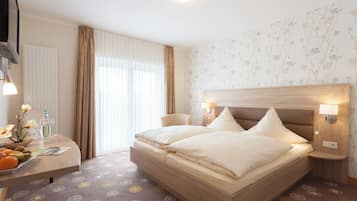 A hotel room with a large bed, bedside tables, a desk with a chair, a radiator, and a window with curtains.