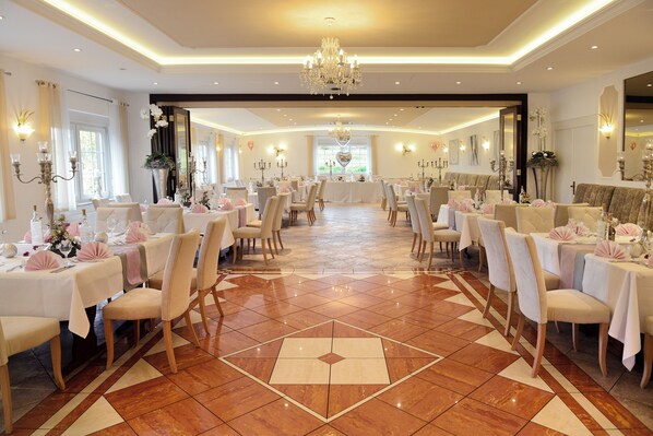 A spacious hotel dining area with multiple tables and chairs, a chandelier, and a polished tile floor. - Hotel Hammermühle (Wahlrod)