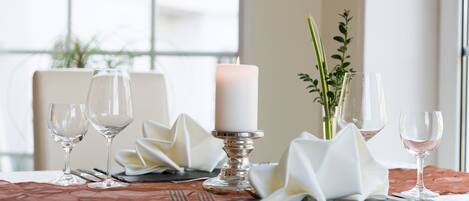A table set for dining with a candle centerpiece, clear glassware, and a decorative napkin arrangement.