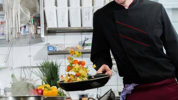 Un chef en una cocina profesional con superficies de acero inoxidable, una olla sobre la estufa y diversos utensilios de cocina.