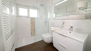 A modern bathroom with a glass shower enclosure, a toilet, a sink with a mirror, and a towel rack.