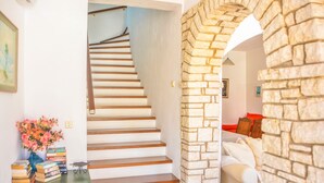 Una escalera de madera lleva a un rellano, con una pared de piedra y un sofá blanco en una habitación bien iluminada.