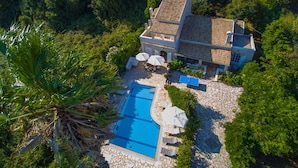 Una casa de dos pisos con una piscina rodeada de baldosas de piedra y follaje.
