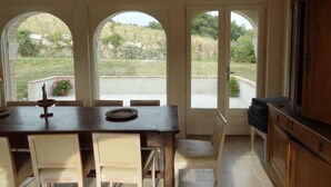 A dining area with a wooden table and chairs, large arched windows, and a view of a garden and hills. - Drôme provençale quiet country house (Cléon-D'andran)