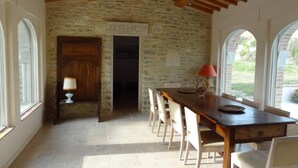 A dining area with a stone wall, wooden ceiling beams, and a long table with chairs. - Drôme provençale quiet country house (Cléon-D'andran)