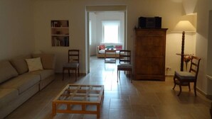 A living room with a sofa, a coffee table, a bookshelf, a cabinet, and a dining area with chairs and a table. - Drôme provençale quiet country house (Cléon-D'andran)