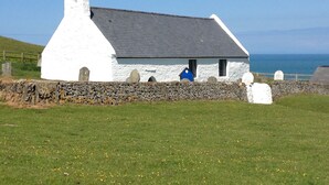 A white building with a grey roof, a stone wall, and a grassy field.