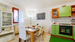 A compact kitchen with a dining area, featuring a wooden table, chairs, a green cabinet, and a tiled backsplash. - Welc-om Green Cottage (Teolo)