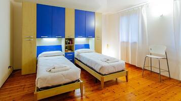 A room with two single beds, wooden flooring, and a white chair.